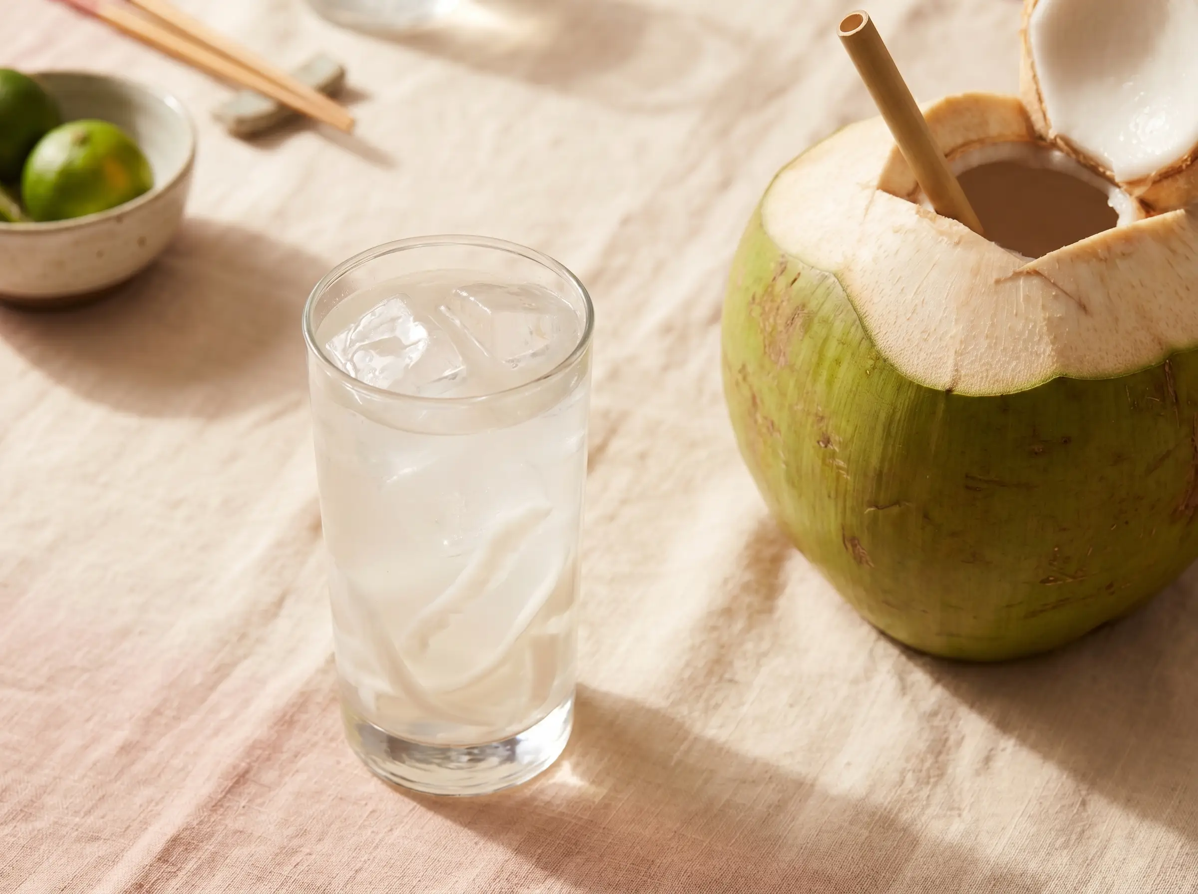 Fresh coconut juice served in a tall glass with a fresh young coconut behind it.